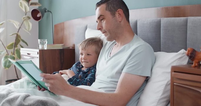Dad reading a book in bed to young boy, bedtime stories daily routine habit