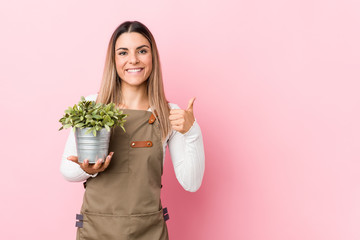 Young gardener woman holding a plant smiling and raising thumb up - Powered by Adobe
