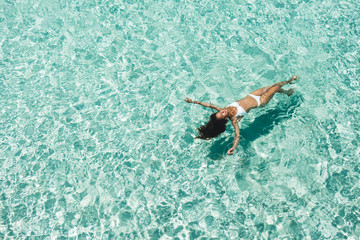 Woman in white bikini lying on transparent turquoise water surface on beach. Travel and vacations concept. Tropical background with empty space - 305307668