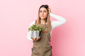 Young gardener woman holding a plant being shocked, she has remembered important meeting.