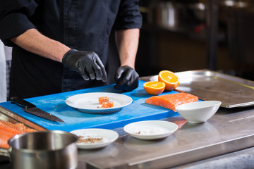 Theme cooking is a profession of cooking. Close-up of a Caucasian man's hand in a restaurant kitchen preparing red fish fillets salmon meat in black latex gloves uniform