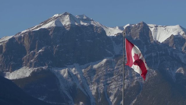 Canadian Flag Blowing in the Wind with Rocky Mountains in the Background, West Coast, Banff, Canmore, Alberta, Canada, Wide Shot on Clear Sunny Day