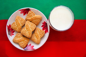 A glass of milk and cookies or shortcake biscuits on the plate with red and green background.  National Cookie Day background. Christmas breakfast for Santa. American breakfast
