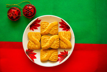 The photo of a pile of  cookies or shortcake biscuits on the plate with red bells.  National Cookie Day background. Christmas breakfast for Santa.