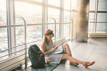 theme of tourism and travel of young student. Beautiful young caucasian girl in dress and hat sits on floor tourist rug inside terminal airport terminal. Waiting room delayed flight, delay departure © Elizaveta