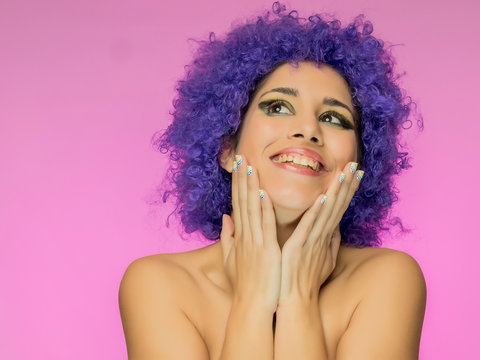 Mujer riendo con peluca morada sobre fondo rosa divirti&eacute;ndose y pas&aacute;ndola bien