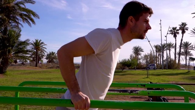 Slow motion, sportsman training on the bars of a park for calisthenics exercises and exercises with his own weight there are palm trees at the bottom of the image
