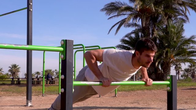 Slow motion of a sportsman doing push-ups on a green park bar for calisthenics and outdoor crossfit there are palm trees at the bottom of the image