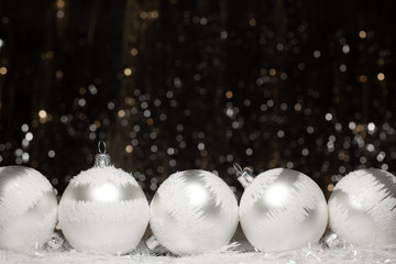 Christmas decorations composition view of five silver evening balls with white snow on it on dark background with silver and gold colors bokeh. Holiday concept with copy space
