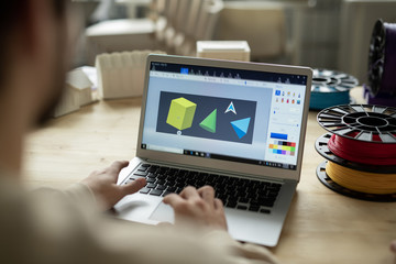 Geometric shapes on laptop display and hands of creative designer working