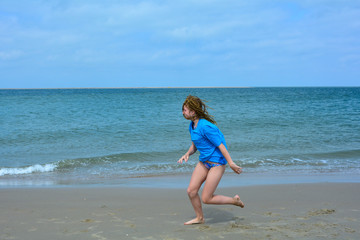 Fototapeta na wymiar Young girl is running at the sand beach, in front of the sea