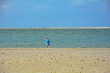 A woman with long hair, from behind, standing by the sea, on the sandy beach,