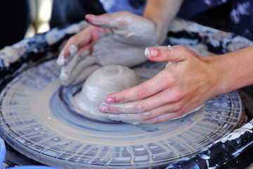 Hands modeling a clay bowl on a turntable.