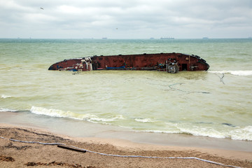 a cargo ship lies on its side, near the shore of a sandy beach with a barrier to the pollution zone after the ship’s wreck.