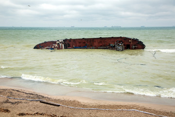 a cargo ship lies on its side, near the shore of a sandy beach with a barrier to the pollution zone...