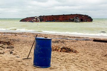 fighting the consequences of a tanker wreck on a sandy beach a protective barrier and a barrel for collecting oil waste.