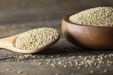 White quinoa seeds in wooden spoon and bowl on rustic background ( Chenopodium quinoa ), cereal healthy vegetarian food gluten free to lose weight