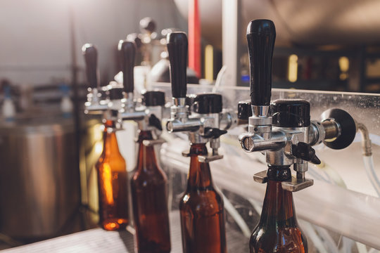 Brewery Factory Spilling Beer Into Glass Bottles On Conveyor Lines. Industrial Work, Automated Production Of Food And Drinks. Technological Work At The Factory.