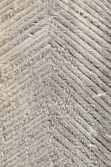 An old stone wall is covered with a rough angled relief with notches. Vertical