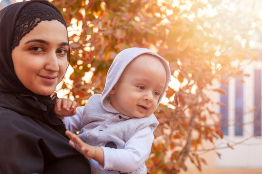 Young Muslim woman in hijab holding her 1-year-old baby boy, hugging and kissing. Happy Muslim mother in abaya clothing kiss and play with her little child