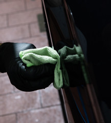 male hand with glove removing a scratch on the outerside of a dark car with a green cloth 