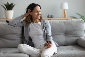 Beautiful woman spend lazy weekend seated on couch with smartphone
