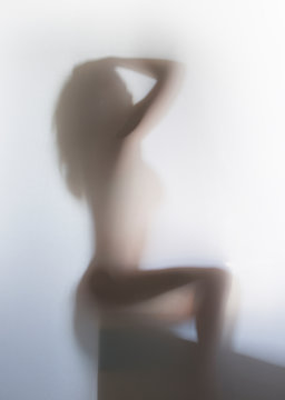 Beautiful and sexy long hair woman sits and poses behind a bathroom curtain. Only body silhouette can be seen.