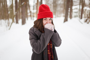 Young woman warming her hands with breath in winter forest looking directly in camera