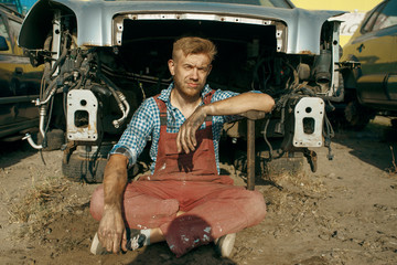 Male mechanic poses on car junkyard