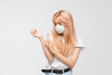 Blonde woman in medical mask scratching hand and looks at the place of itchy. Dry sensitive skin, allergy symptoms, dermatitis, insect bites. Irritation concept. Isolated on white background.