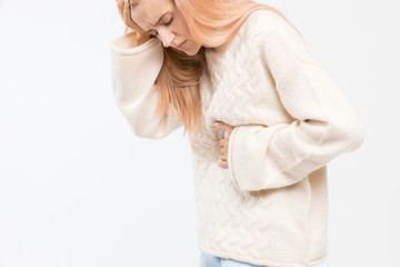 Naklejka premium Cropped studio portrait of woman in white sweater suffering from abdominal pain, having menstruation pain, stomach ache. Girl feels bad. Menstrual period, gynecology, gastritis. Healthcare concept.