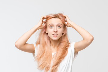 Fototapeta premium Close up studio portrait of young pretty blonde girl in white t-shirt. Woman raised hand to her hair and look at camera. An exclamation of surprise. Stunned puzzled female. Emotions concept.