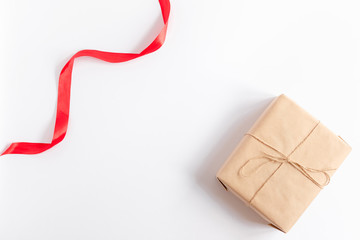 Preparation for Christmas holidays. Red ribbon and gift box in craft wrapping paper with jute rope. White background, flat lay. Merry Christmas and Happy New Year concept. Nativity mood. Close up.