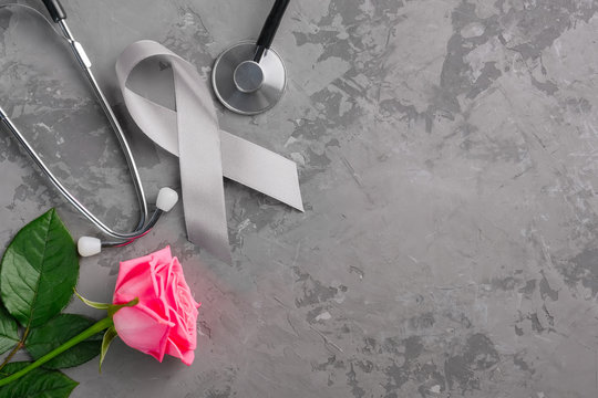 Grey ribbon, stethoscope and pink rose on a concrete background. Parkinson's disease or brain cancer awareness concept