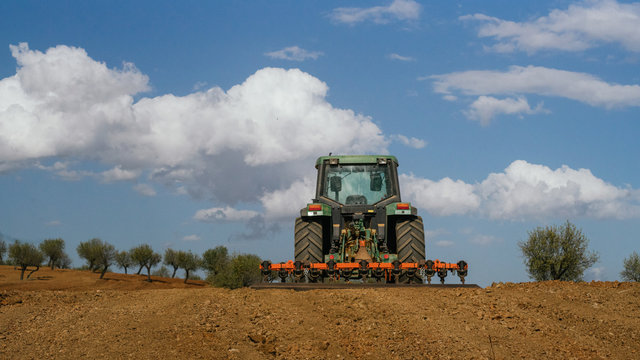 Tractor verde labrando un campo de almendros con nubes