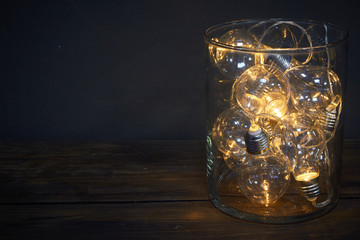 Glass vase filled with luminous bulbs on a wooden table, holiday concept