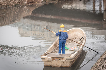 Back view a woman working on the boat cleaning up a polluted river in Hanoi, Vietnam