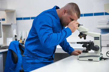 Production lab employee man looking through a microscope