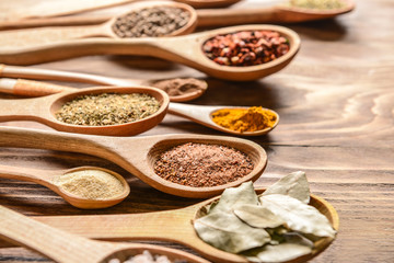 Spoons with different spices on wooden background, closeup