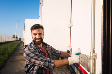 Smiling truck driver. trucker in working gloves opening or closing truck trailer back doors...