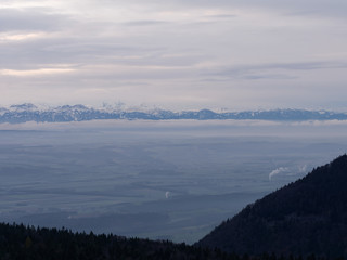 Winter landscape at sunrise. Silhouette of hills and trees in the foreground and snow capped mountain range of the European alps in the background.
