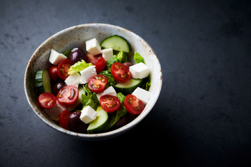 Fototapeta na wymiar Salad with Kalamata Olives, Cucumber Cherry Tomatoes and Feta Cheese on black Stone Background. Healthy Snack Idea. Close up.