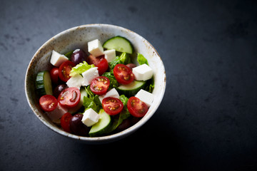 Salad with Kalamata Olives, Cucumber Cherry Tomatoes and Feta Cheese on black Stone Background. Healthy Snack Idea. Close up.