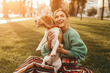 Joyful woman on grass holding dog tight and looking up