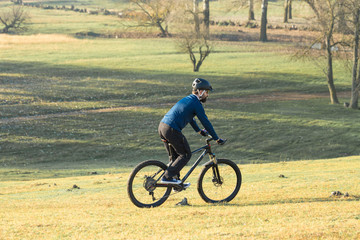 Fototapeta premium Cyclist in pants and fleece jacket on a modern carbon hardtail bike with an air suspension fork. The guy on the top of the hill rides a bike.