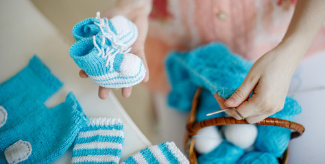 Pregnant woman knits baby clothes on the needles. Booties in the hands.