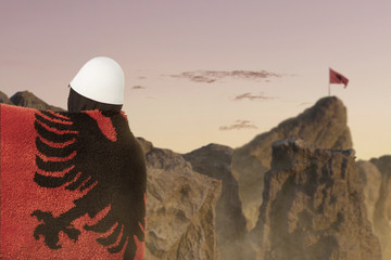side view of man covered with fluffy albanian flag in front of blurred mountains to celebrate....