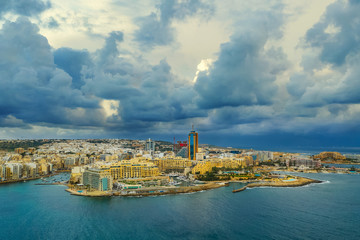 Fototapeta premium Aerial view of Saint Julian's city and Portomaso tower. Winter, sea, seafront, cloudy blue sky. Malta island