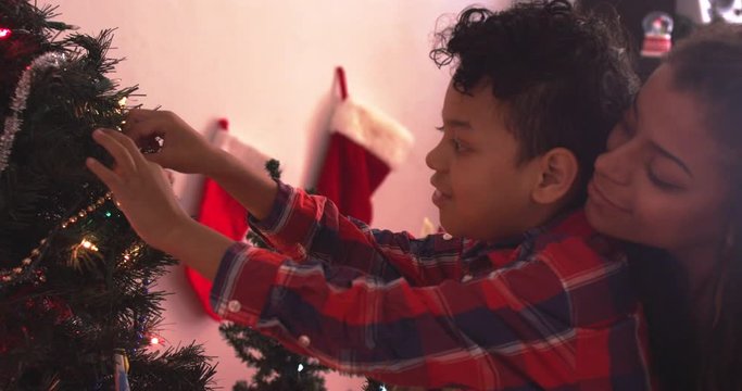 Mom lifting up son to hang a sparkling ornament on the Christmas tree - mixed - slow motion - shot on RED