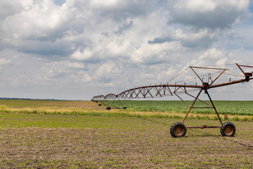 Rusty, old center pivot irrigation system stretching over rolling hills between soybean and corn farm fields. sunny summer day with clouds